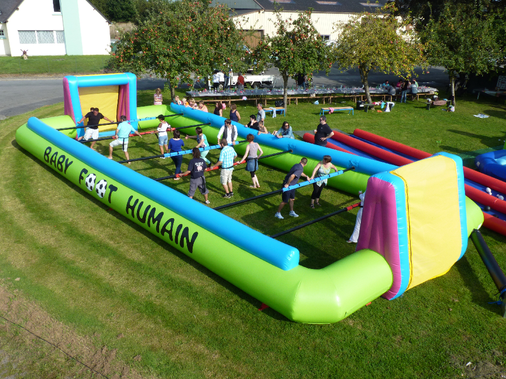 Une grande structure gonflable colorée pour jouer au babyfoot humain avec des participants actifs, en plein air sur un terrain en herbe.